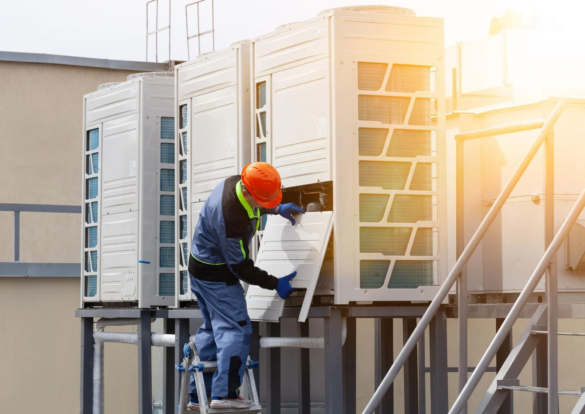 A man is working on an air conditioner on the roof of a building.